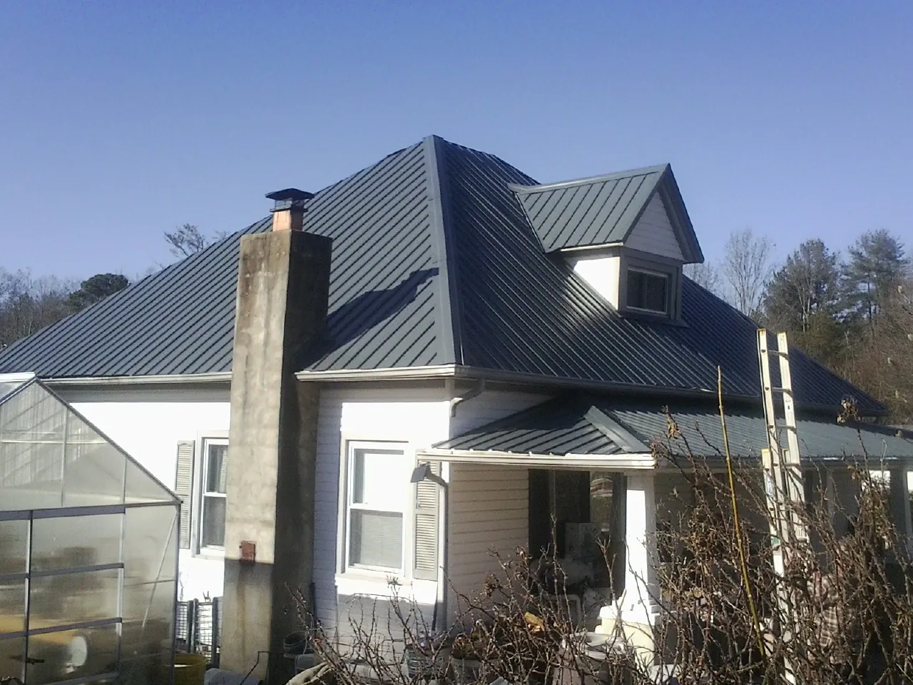 Dark blue standing seam metal roof on a white farmhouse with dormer — Slate & Tile Roof Repair by Roofing Brothers in Midway