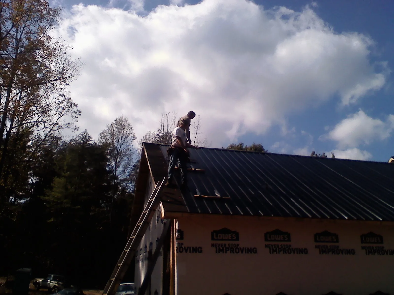 Roofer fastening dark metal panels high against a cloudy sky, from a Roof Inspection job in Midway